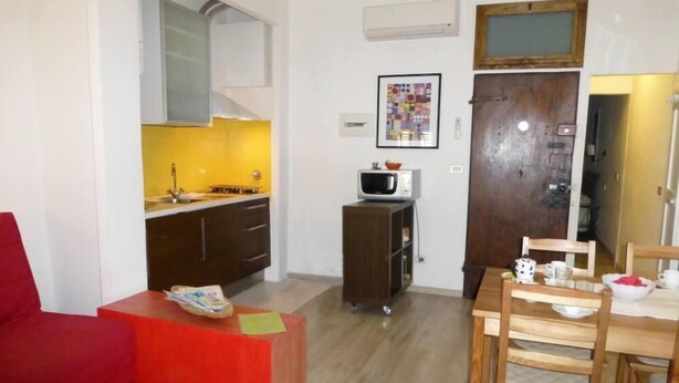 Un espacio habitable compacto con kitchenette, comedor y un sofá rojo.