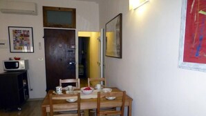 Un comedor con una mesa y sillas de madera, un microondas en un mueble y cuadros en las paredes.