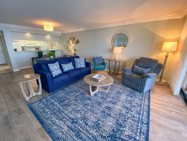 Ein Wohnzimmer mit einem blauen Sofa, einem grauen Sessel, einem Couchtisch und einem gemusterten Teppich.
