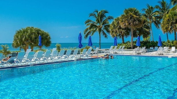 A poolside area with lounge chairs and umbrellas, palm trees, and a clear blue sky. - Key West Beachfront Luxury 2/2 Condo A212   (Key West)