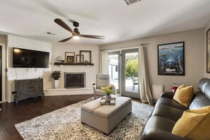 A living room with a fireplace, a ceiling fan, a sofa, and a large TV. - Pool House Scottsdale | Play Starts Here! (Scottsdale)