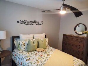 Quarto com cama, penteadeira, ventilador de teto, decoração de parede e espelho.