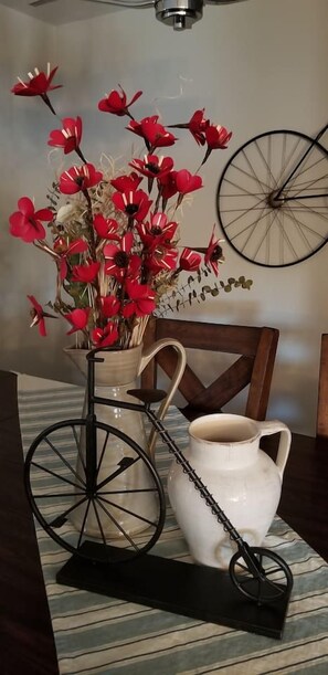 Een eettafel met een vaas rode bloemen, een witte karaf en een fietswiel.