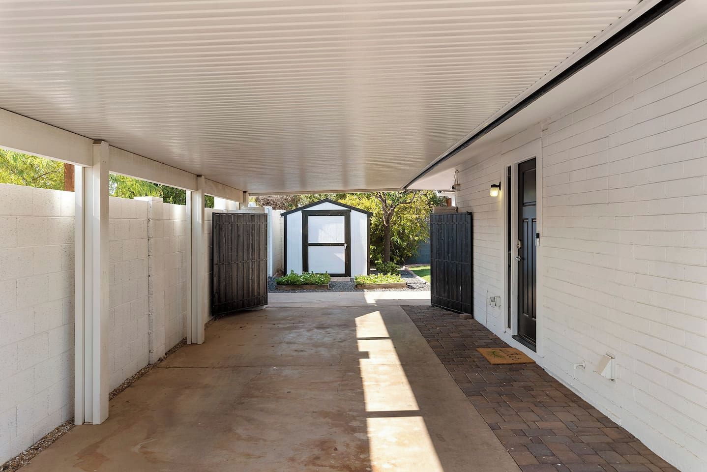 A covered outdoor corridor with a concrete floor, white walls, and a wooden fence on one side.