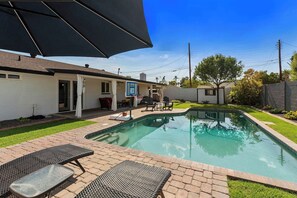 Piscina com área de terraço, incluindo espreguiçadeiras e um espaço de estar coberto.