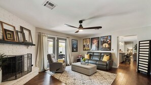 A spacious living room with a fireplace, a ceiling fan, and a large window. - Old Town Scottsdale All around VACATION experience! Heated Pool & Media Room (Scottsdale)