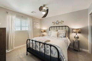 Une chambre à coucher avec un lit, des lampes de chevet, un ventilateur de plafond et une fenêtre avec des rideaux.