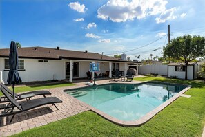 Un patio trasero con piscina, sillas de descanso y aro de baloncesto.