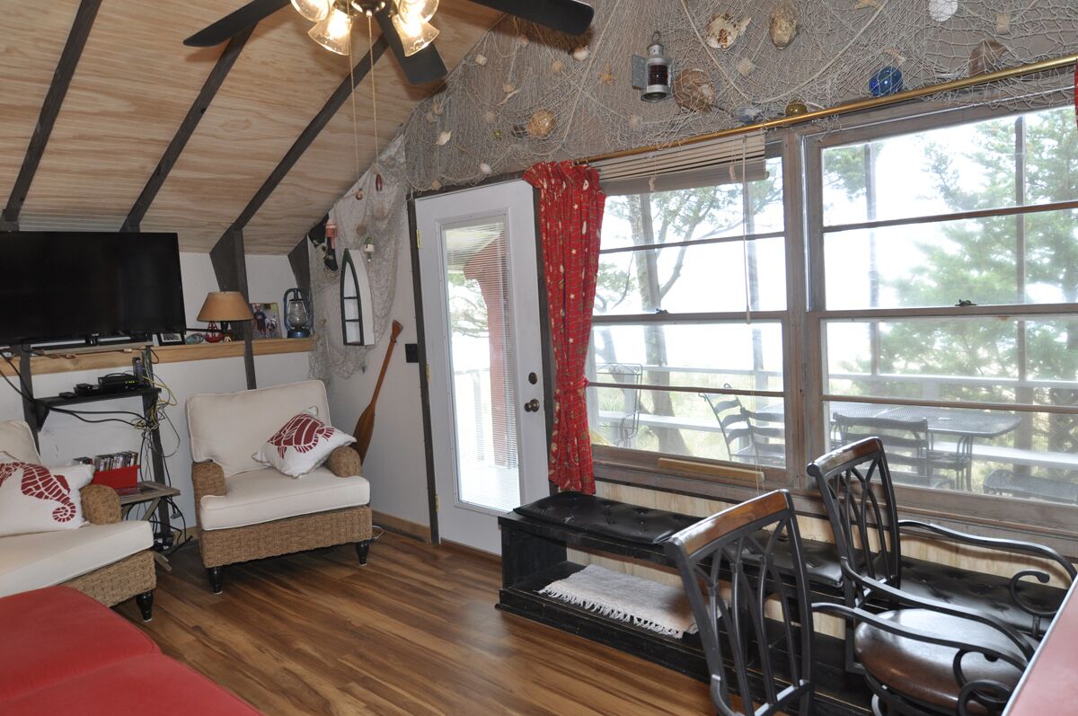 Una habitación acogedora con techo de madera, un sofá, una mesa de comedor con sillas y un amplio ventanal con cortinas rojas.