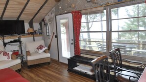 Ein gemütliches Zimmer mit Holzbalkendecke, einer Couch, einem Esstisch mit Stühlen und einem großen Fenster mit roten Vorhängen.