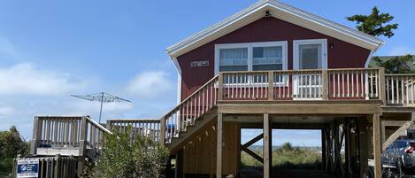 A two-story wooden house with a balcony, a rental sign, and a clear sky.