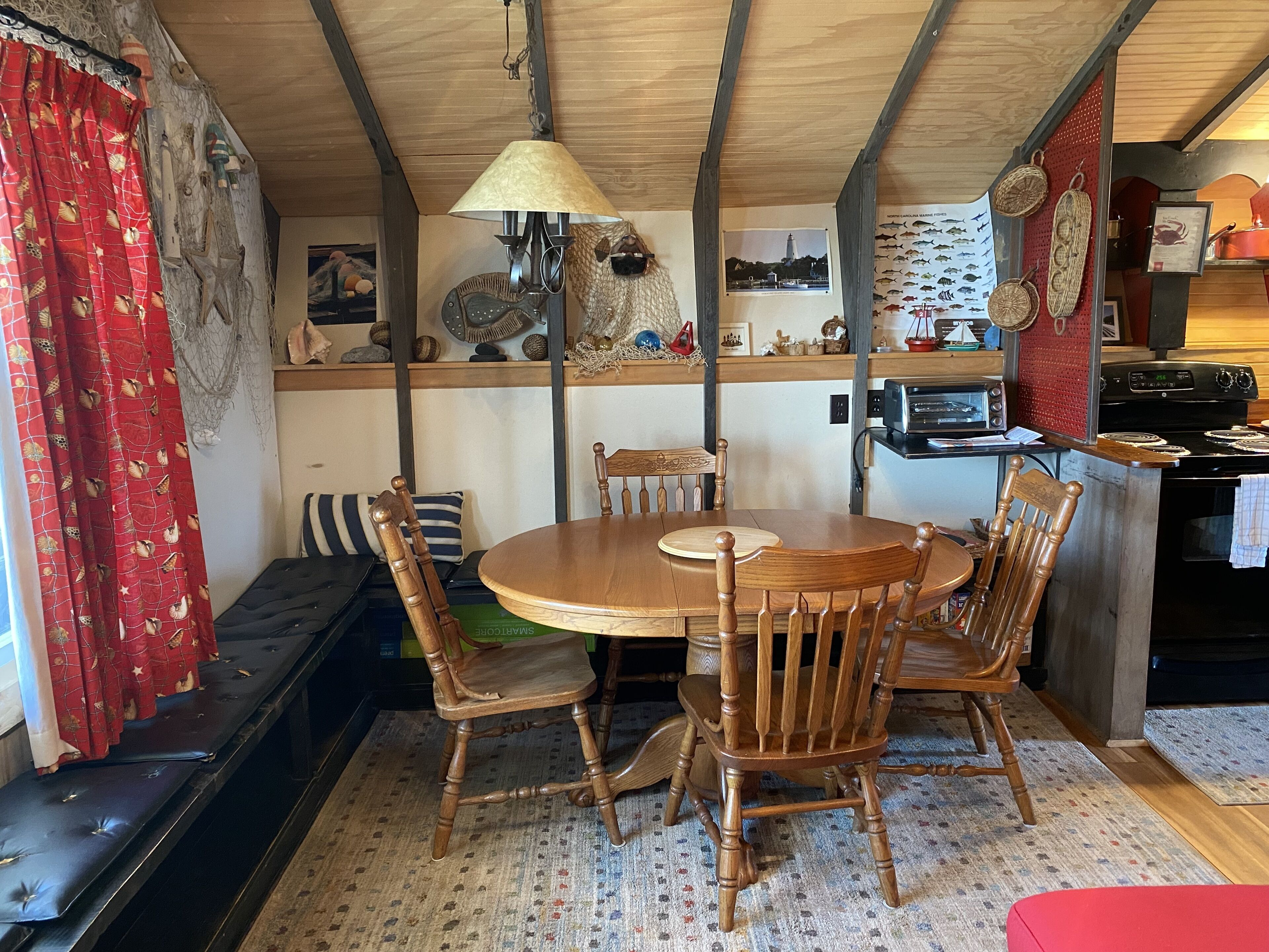 Un coin repas accueillant avec une table et des chaises en bois, un banc, et un espace cuisine équipé d’une cuisinière et d’un grille-pain.
