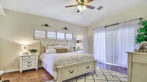 A bedroom with a bed, nightstands, a ceiling fan, a window with blinds, and a large window with curtains.
