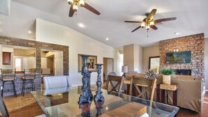A spacious living room with a glass-top dining table, two ornate vases, a fireplace, and a ceiling fan.