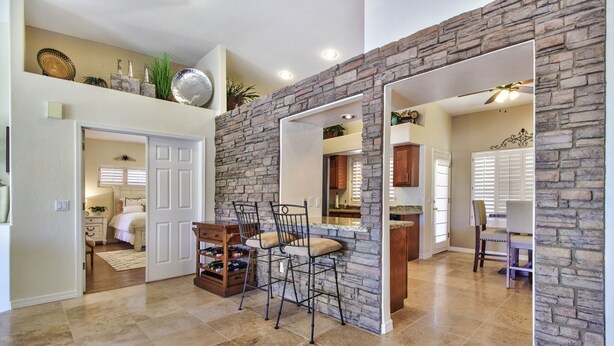 A spacious kitchen with a stone accent wall, a dining area with bar stools, and a view into the adjacent bedroom.
