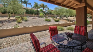An outdoor patio with a round table and striped chairs, surrounded by a landscaped garden with various plants and a view of distant buildings.