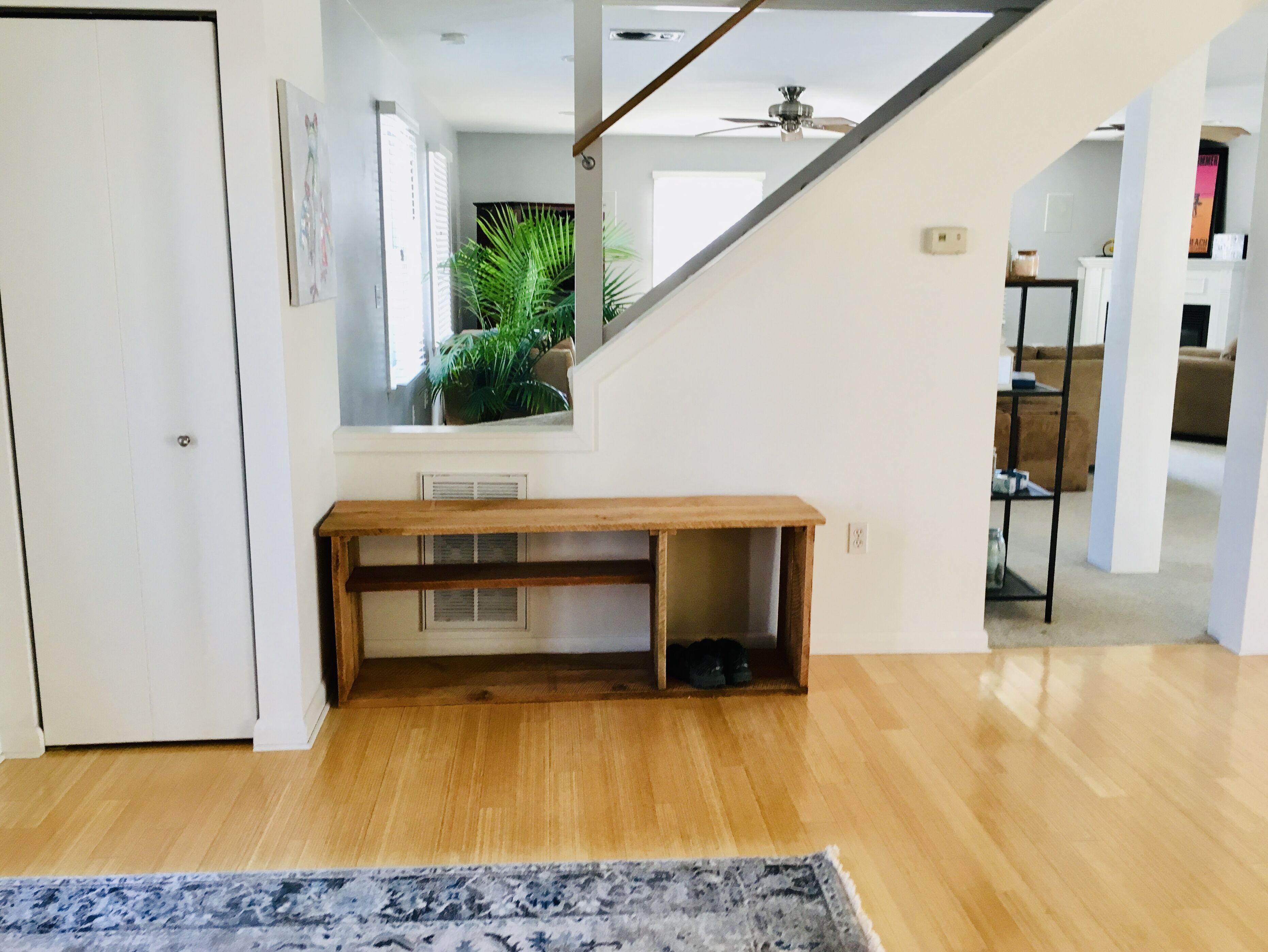 A spacious living area with a wooden bench, a staircase, and a view of a kitchen area.