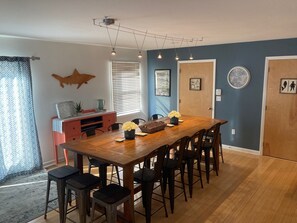 A dining area with a wooden table and chairs, a red entertainment unit, and a large window with blinds.
