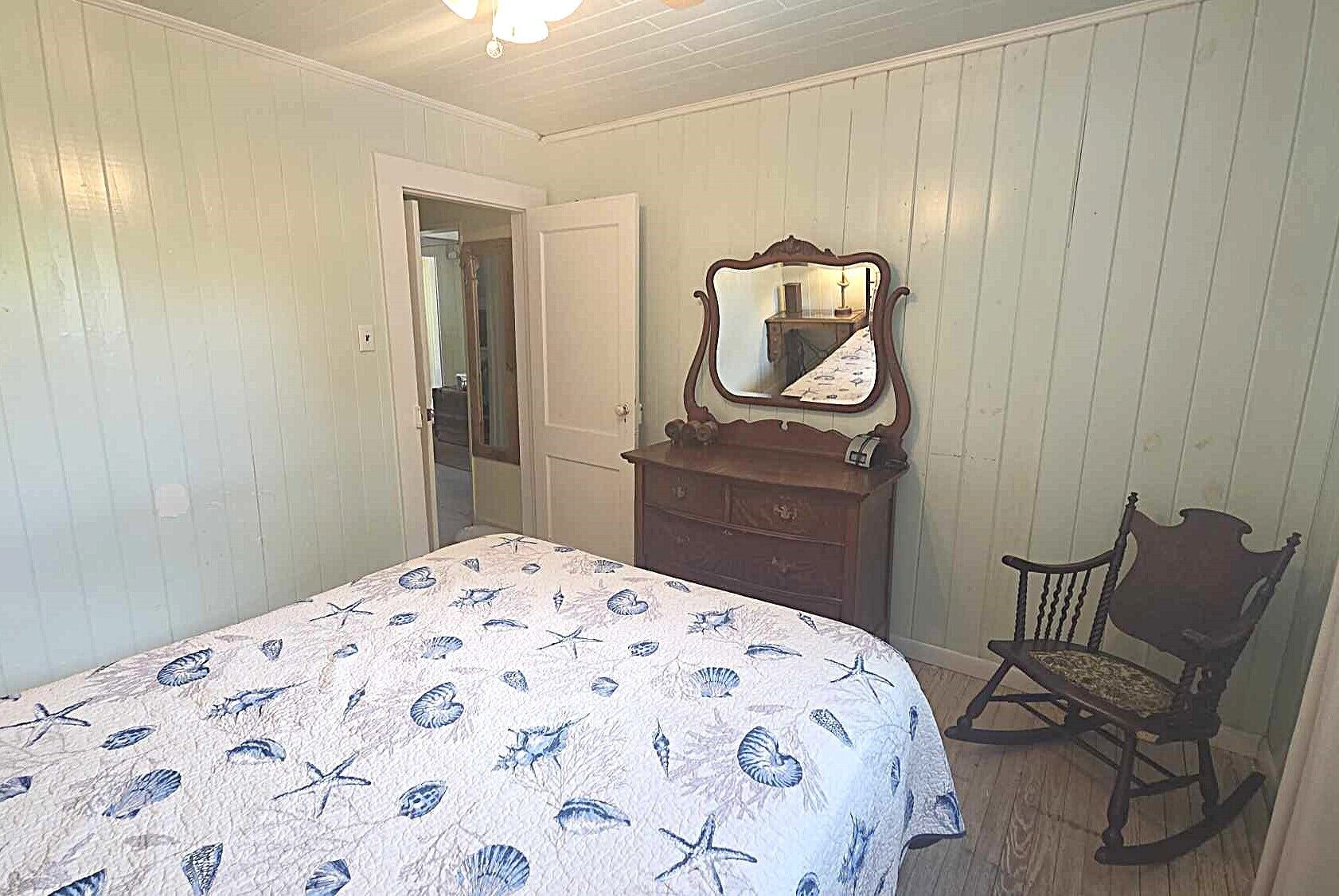 A bedroom with a bed, dresser, mirror, and rocking chair.