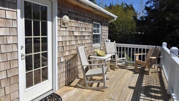Une terrasse en bois avec une balustrade blanche, une porte et deux fauteuils à bascule.