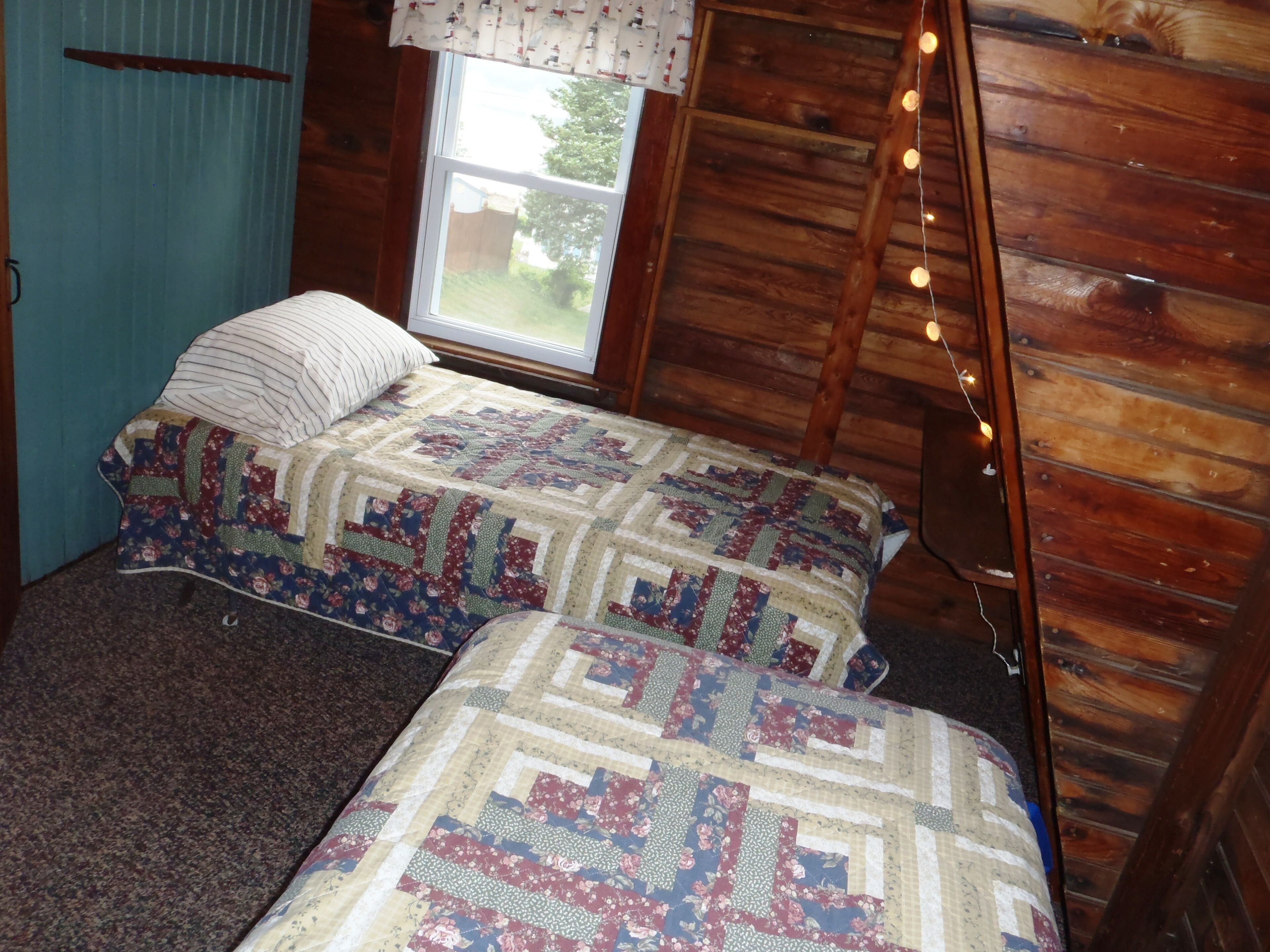 A cozy room with a wooden interior, a bed with a floral quilt, a window with a view, and string lights.