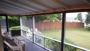 A covered patio with wicker furniture and a view of a backyard.