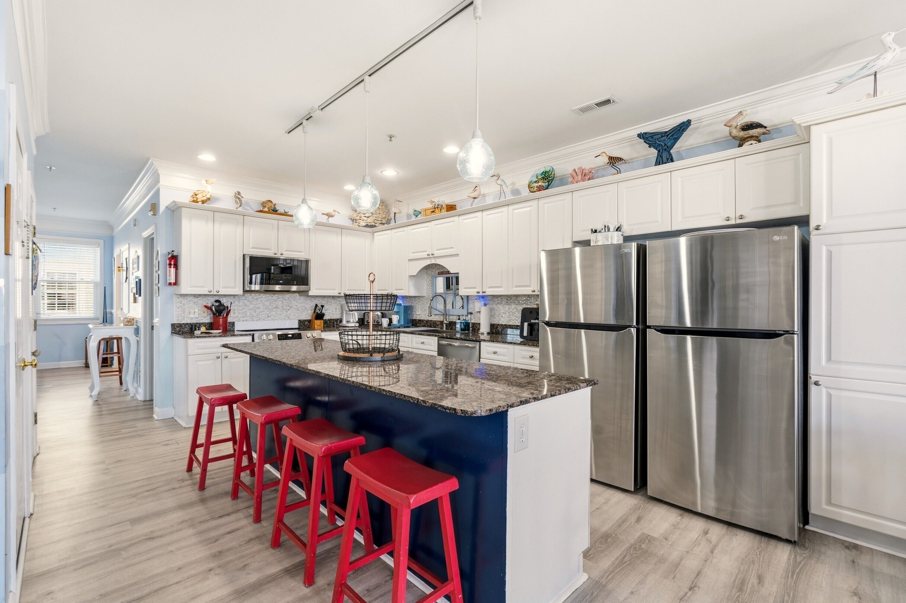 Una cocina moderna con armarios blancos, electrodomésticos de acero inoxidable y una isla central con taburetes rojos.