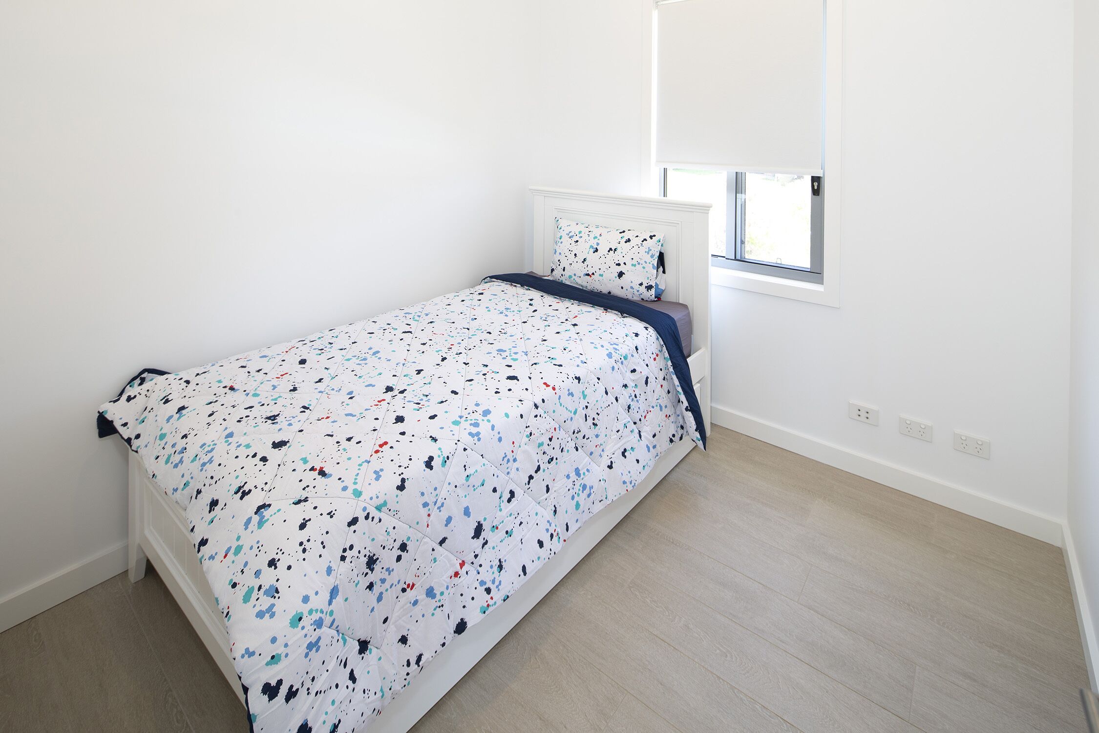 Une petite chambre à coucher, bien rangée, avec un lit, une fenêtre et une prise électrique au mur.