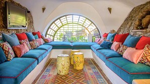 A cozy room with a large arched window, a blue sofa set, colorful cushions, and two decorative vases on the floor.