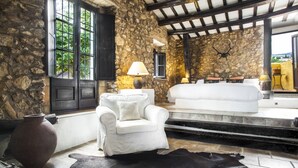 A stone-walled room with a white sofa, a white armchair, and a leather rug.