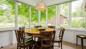 A dining area with a round wooden table and chairs, large windows with a view of greenery, and a hanging light fixture. - (Aug 08-14 open!) LAKESIDE HOME CLOSE TO PRIVATE ASSOCIATION BEACH! (Lakeside)