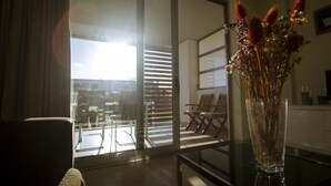 Een kamer met een groot raam, een vaas met gedroogde bloemen en een stoel.