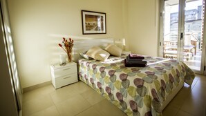 Een slaapkamer met een bed, een nachtkastje, een vaas met bloemen en een lijst met een afbeelding aan de muur.