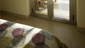 Een kamer met een groot raam dat voorzien is van zonwering, een houten bankje en een gewatteerde spreideken.
