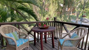 A wooden deck with wicker chairs and a small round table with a flower vase. - Located among the woods on a “country“ road leading West Bay Beach (Roatan)