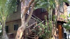 A wooden house with a staircase leading to a porch, surrounded by palm trees and a garden. - Located among the woods on a “country“ road leading West Bay Beach (Roatan)