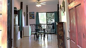A hallway with a dining area, ceiling fans, a refrigerator, and a door with decorative panels. - Located among the woods on a “country“ road leading West Bay Beach (Roatan)