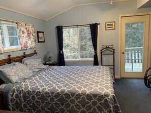 A bedroom with a bed, a nightstand, a window with curtains, a door with a view, and a wooden chair.