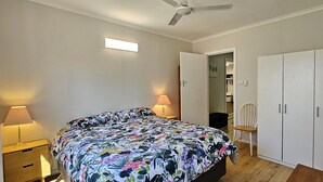 Un dormitorio con cama, lámparas de noche, ventilador de techo, armario y una silla.