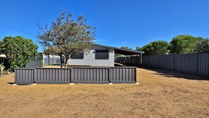 Propiedad residencial con patio cercado, un árbol y una casa con garaje.