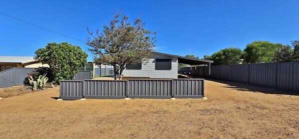 A residential property with a fenced yard, a tree, and a house with a garage. - Patrick Crescent 18 - Kalbarri, WA (Kalbarri)