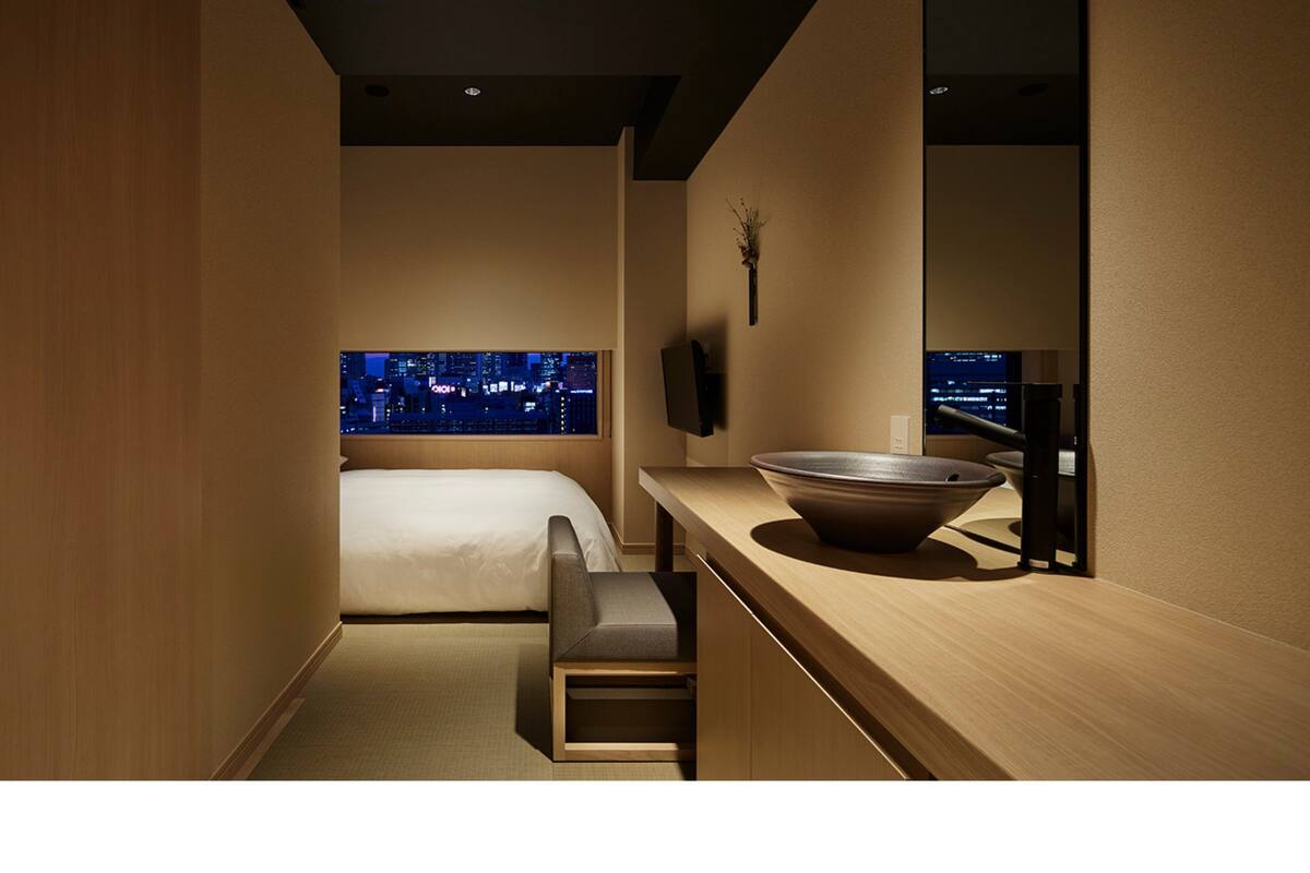 Een moderne hotelkamer met een bed, een zithoekje, een grote spiegel en uitzicht op de stad 's nachts.
