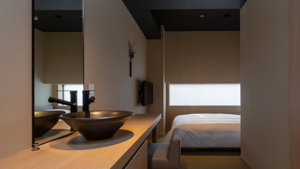 A modern room with a large mirror, a wooden countertop with a bowl, a bed, and a window.