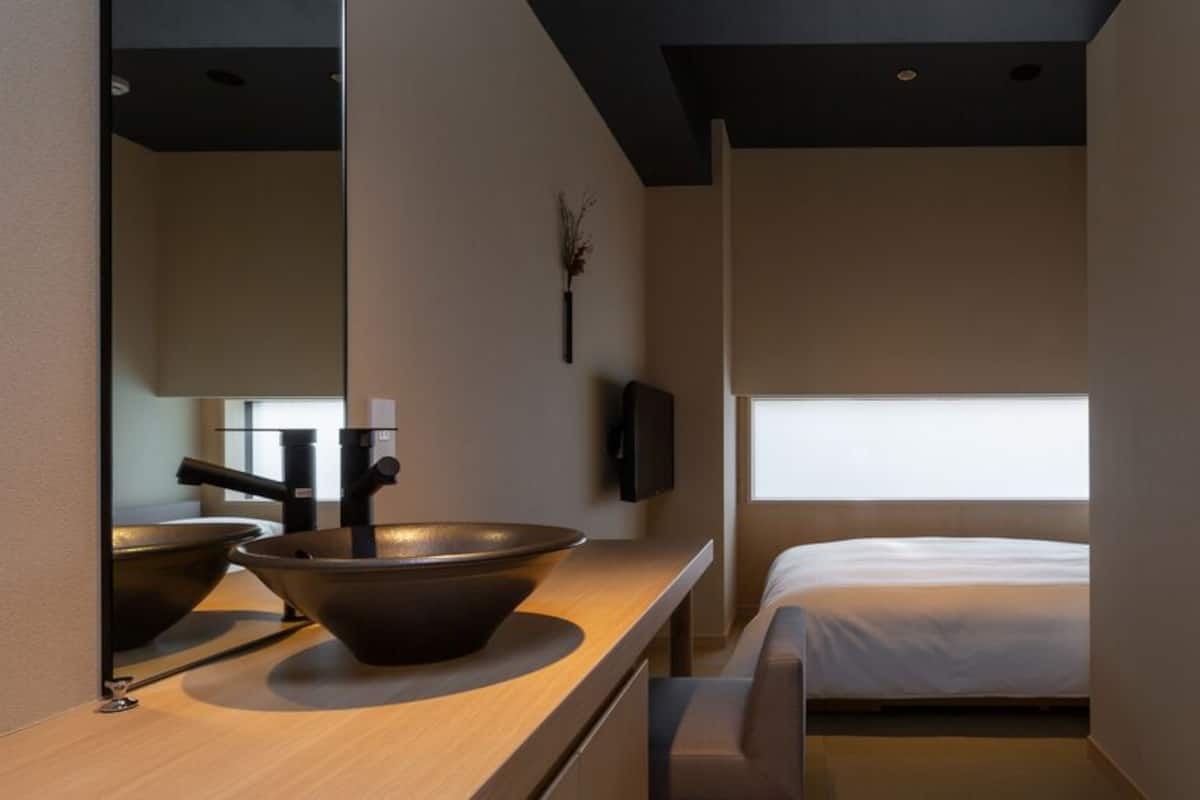 Een moderne kamer met een grote spiegel, een houten aanrecht met een kom, een bed en een raam.