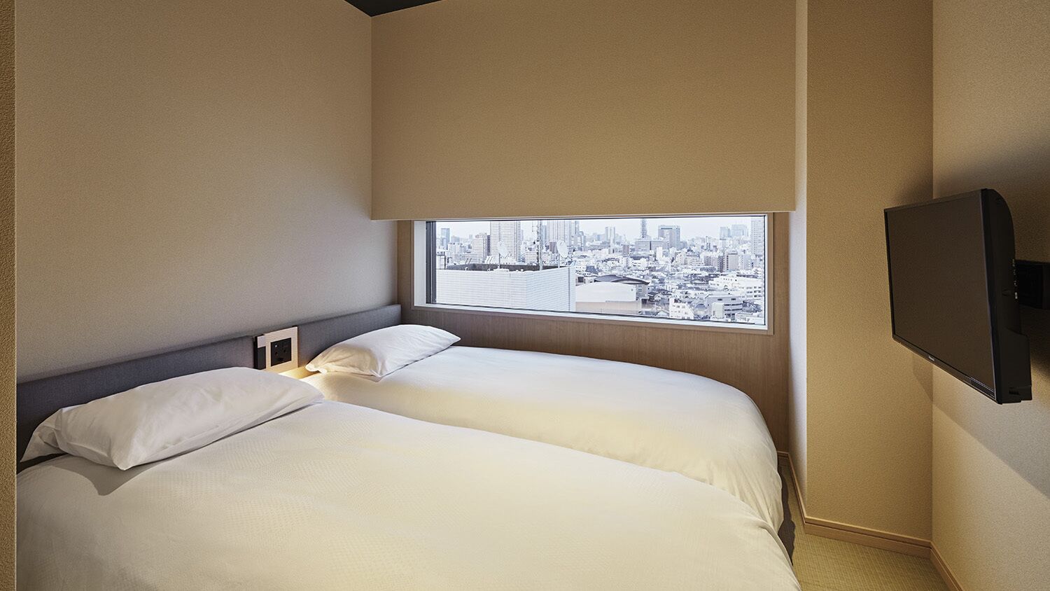 A hotel room with two beds, a city view, and a flat-screen TV.