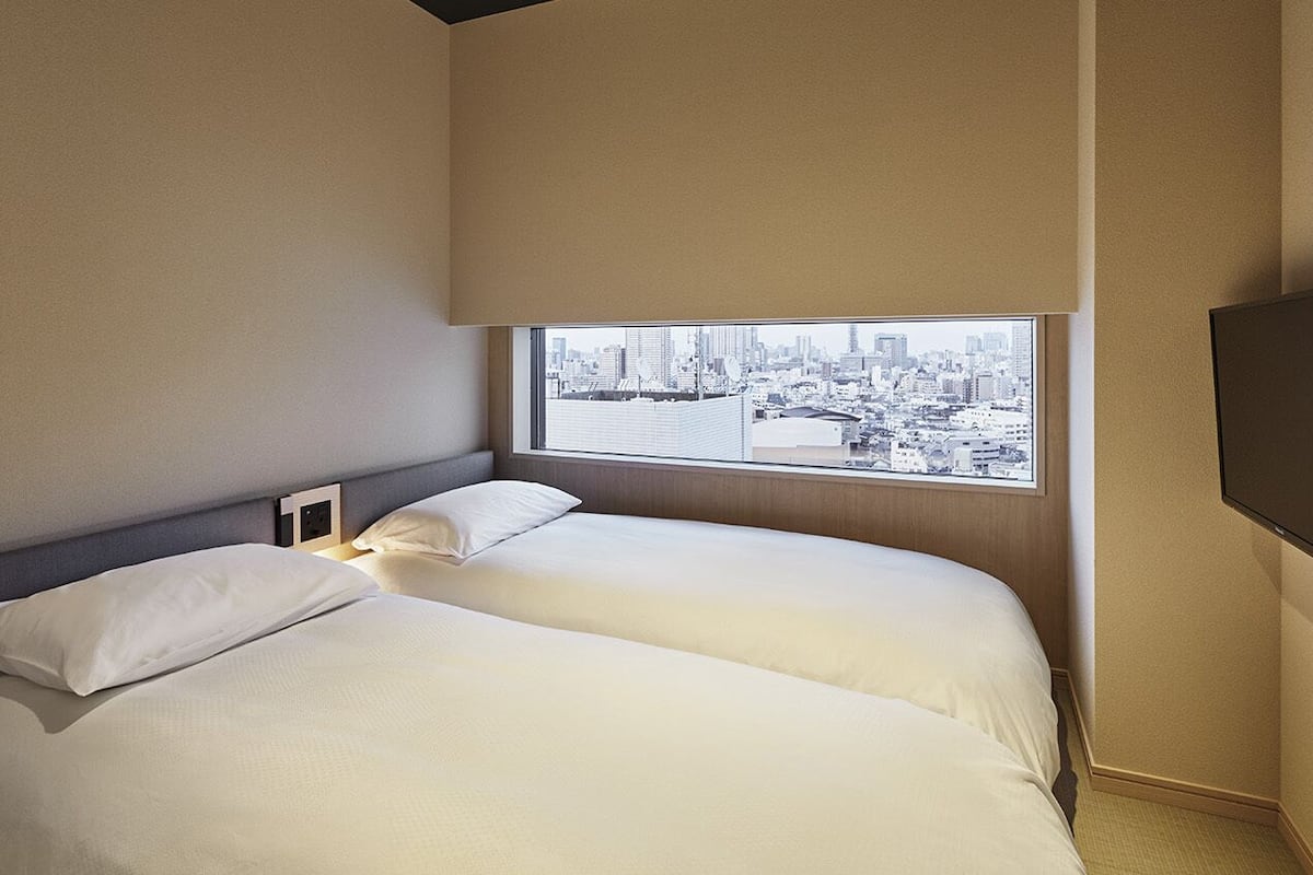Een hotelkamer met twee bedden, uitzicht over de stad en een flatscreen televisie.