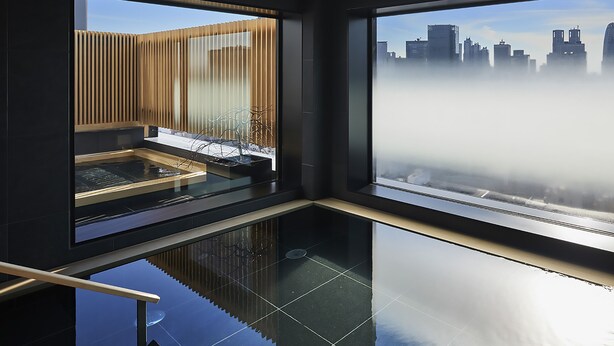 Un interior moderno con ventanas amplias, un suelo reflectante y vistas de un paisaje urbano a través de una ventana brumosa.