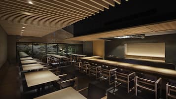 Un restaurante moderno con una barra larga, varias mesas y una pantalla grande.