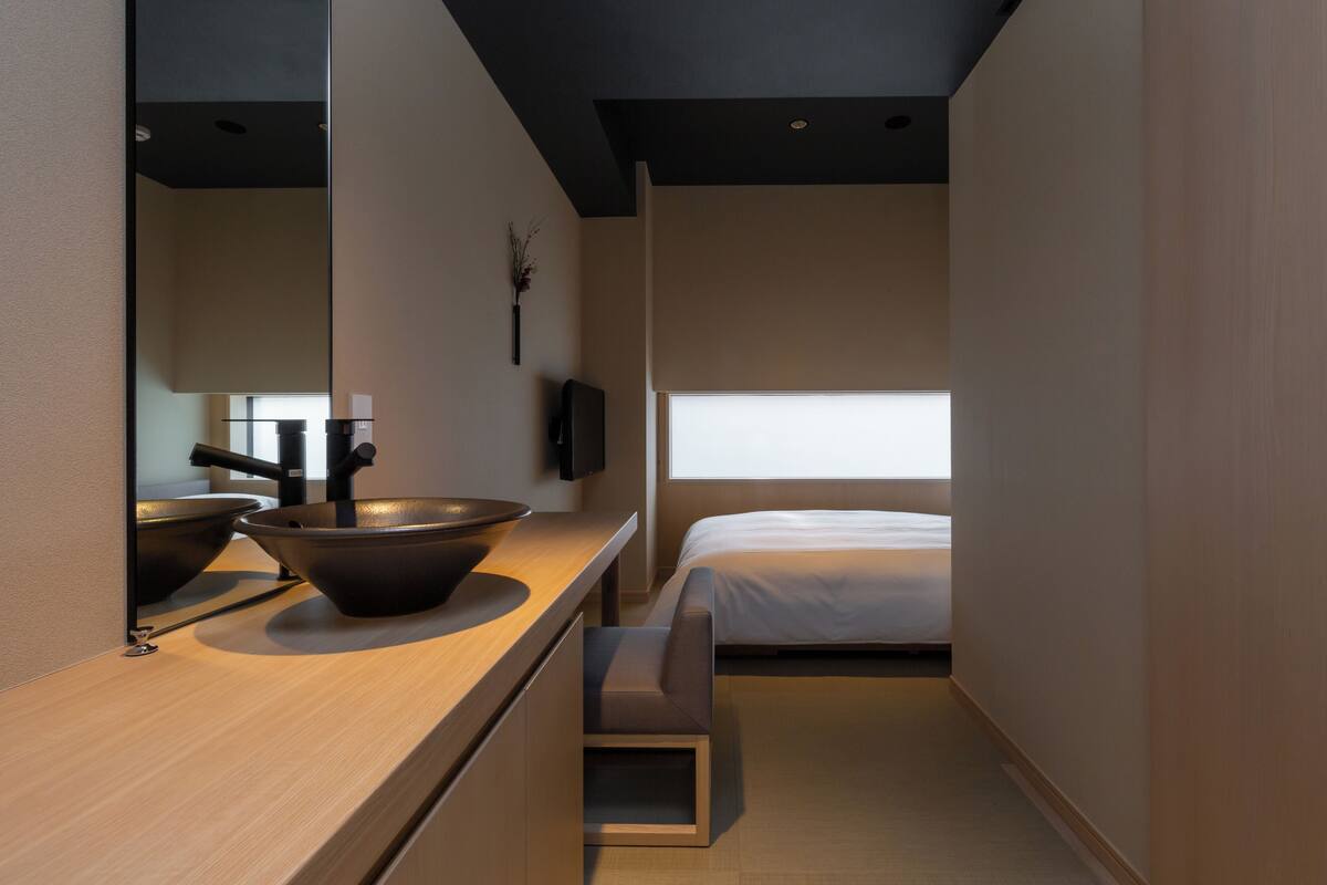 Een compacte hotelkamer met een modern design, met een grote spiegel, een wastafel, een bed en een raam dat natuurlijk licht biedt.