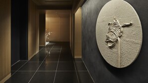 Un pasillo con suelo de baldosas oscuras, paredes de madera y una gran escultura en la pared.